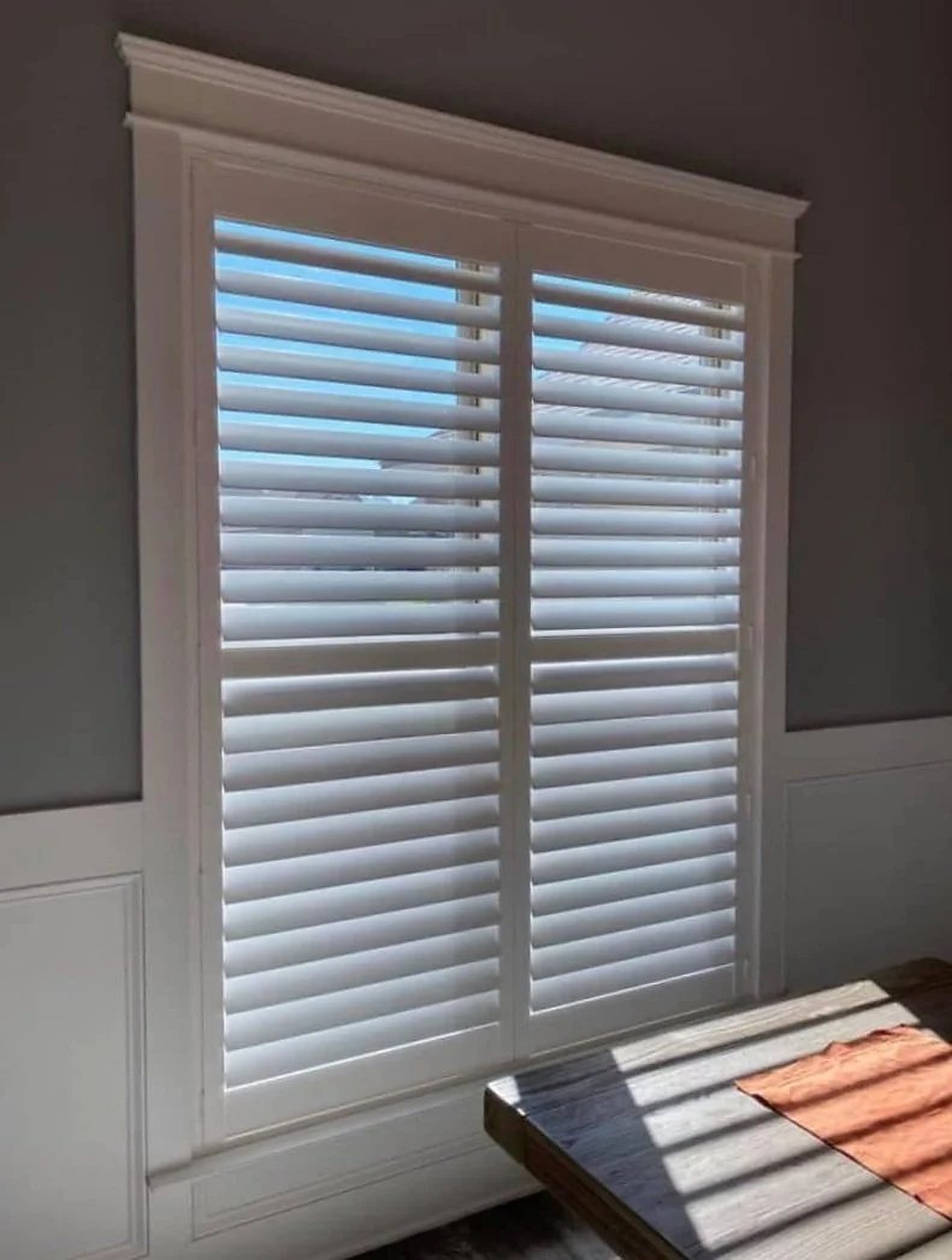 White plantation shutters casting striped light on a wood table