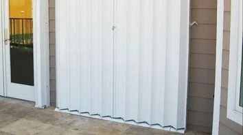 White accordion hurricane shutters stacked beside a window opening