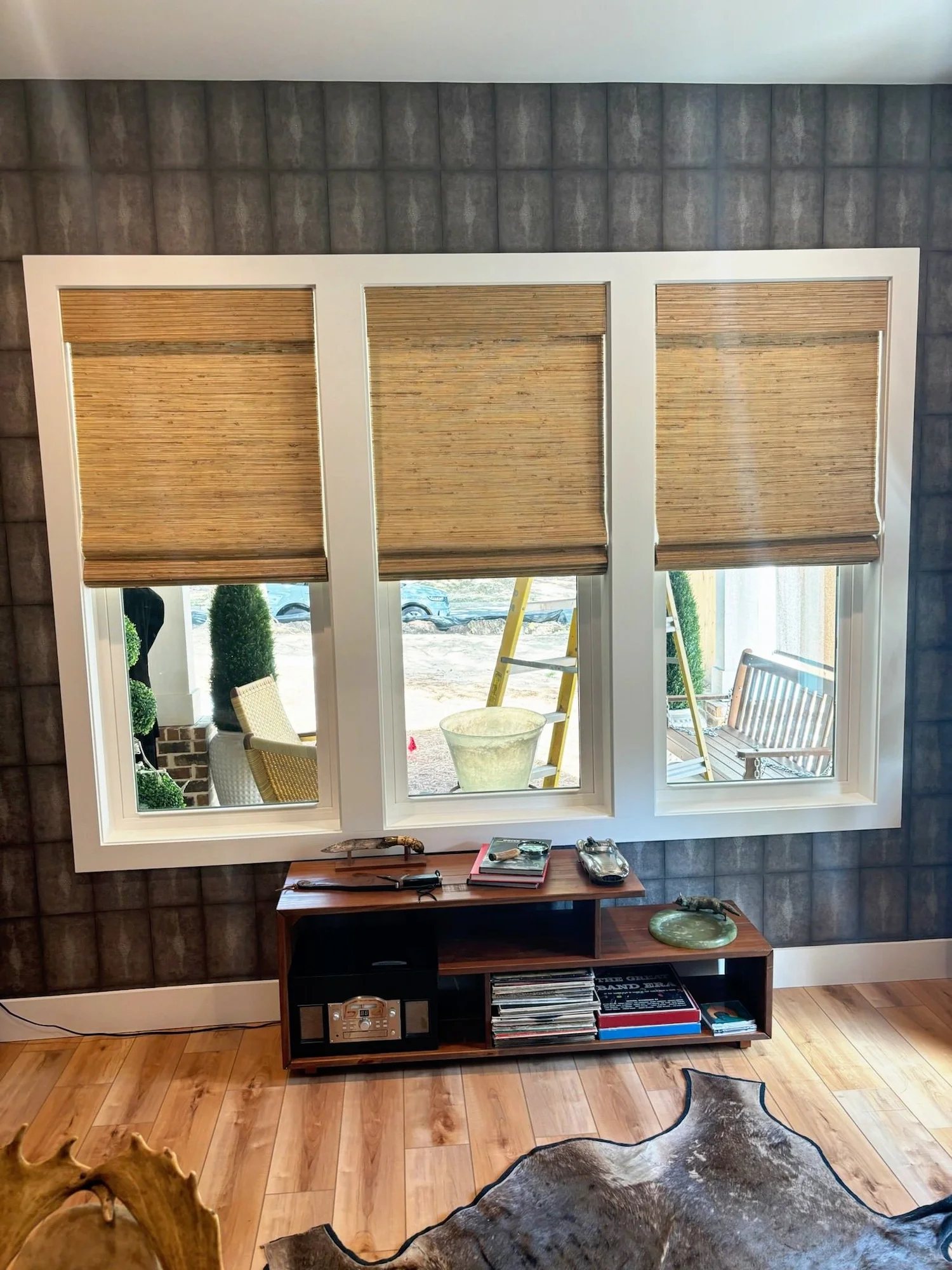 Living room with three windows in woven grass shades above a wood console